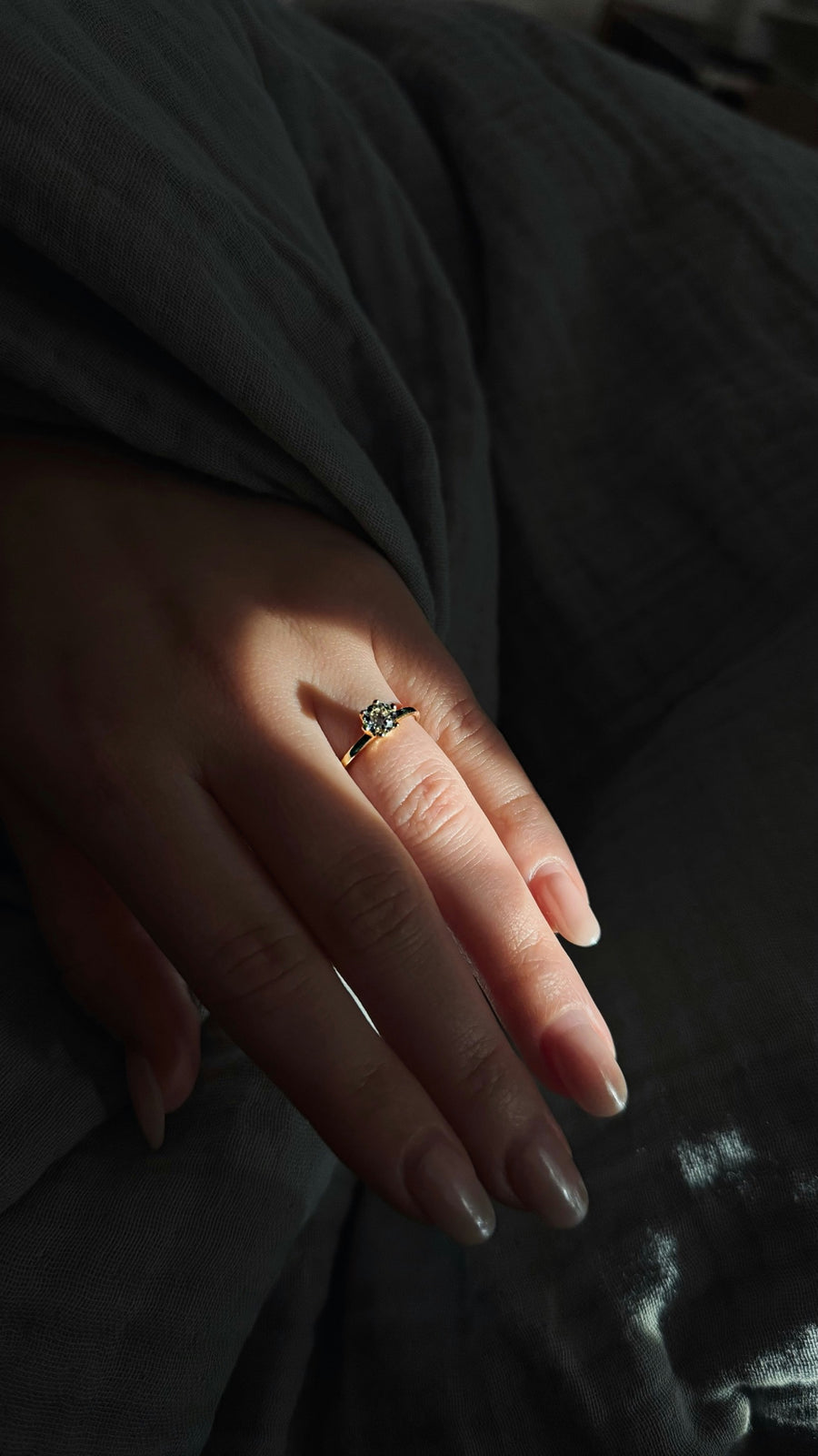 A yellow gold diamond solitaire worn on a hand in soft daylight