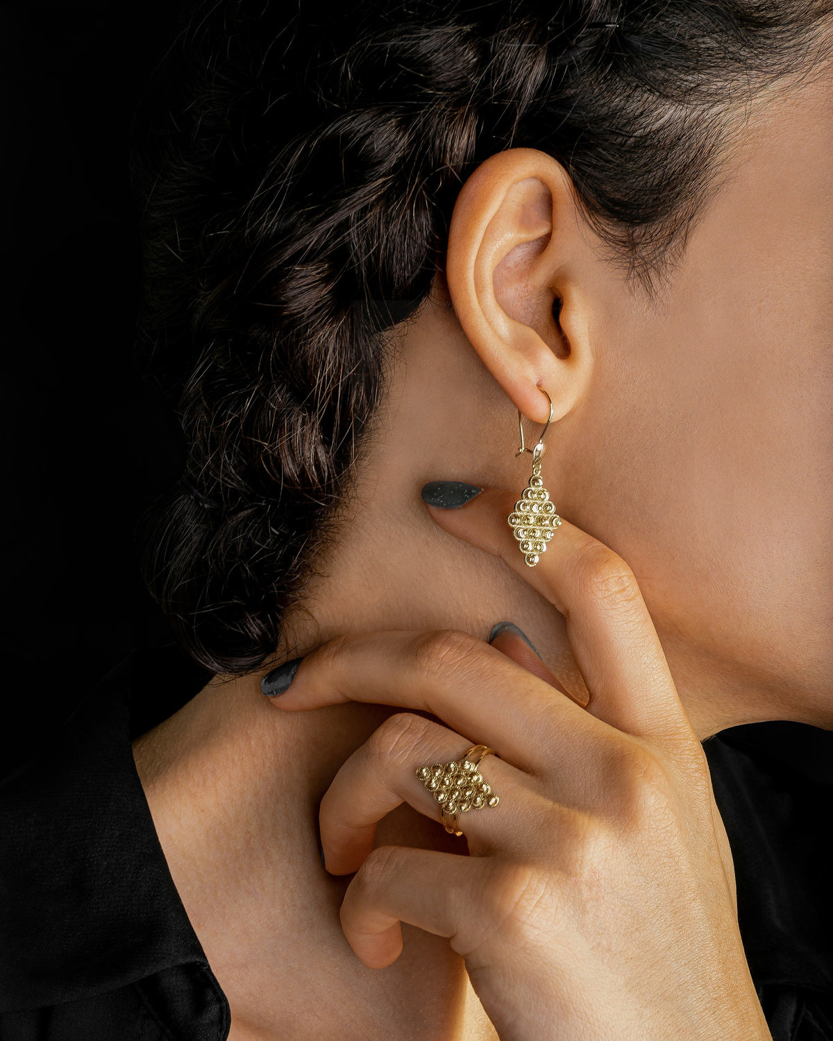 A gold drop earring worn against a dark background