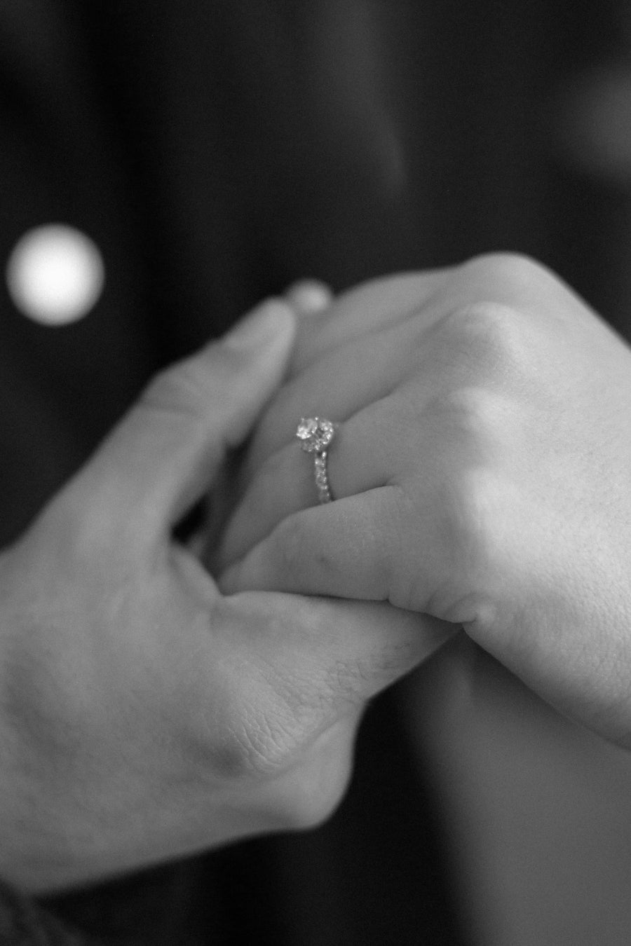 Two hands held together, one wearing a diamond engagement ring, photographed in black and white